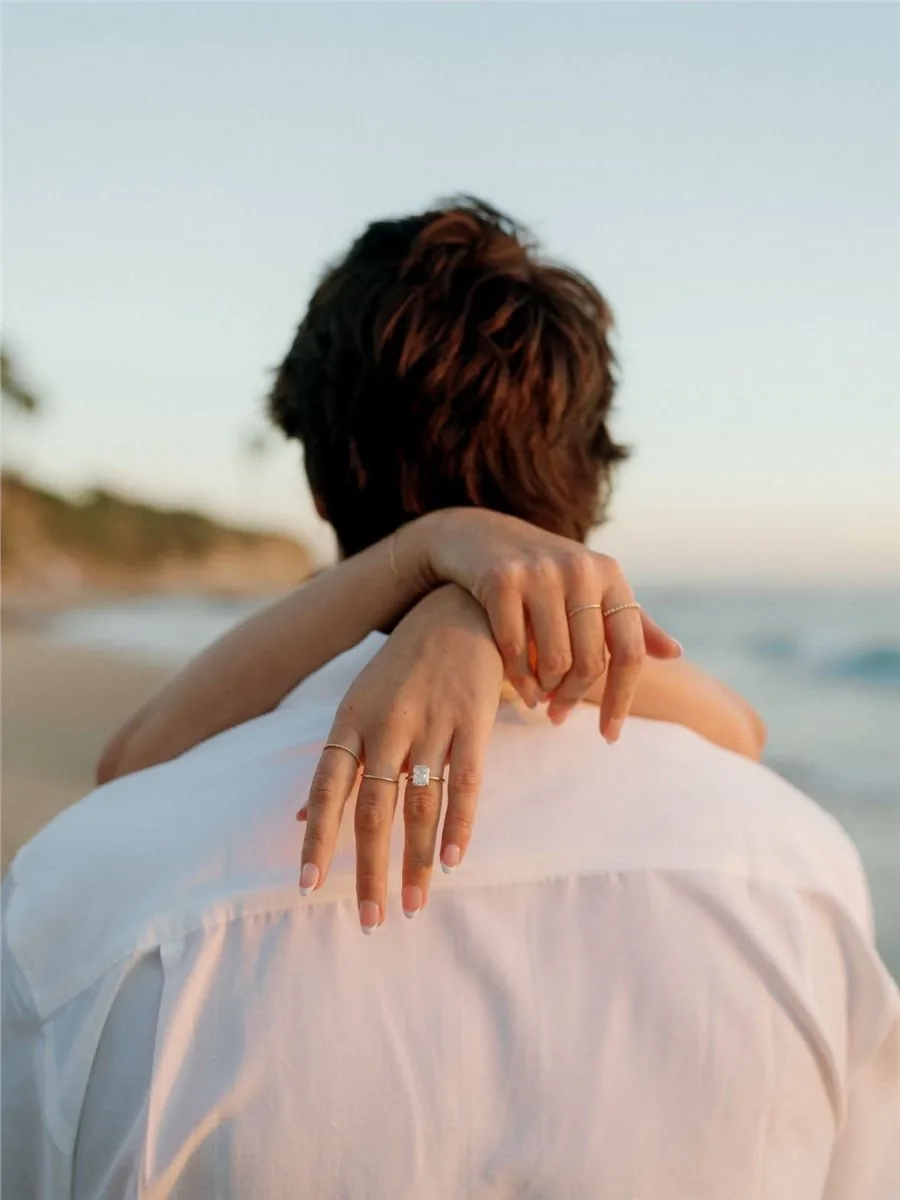 Couple embracing at sunset with an engagement ring